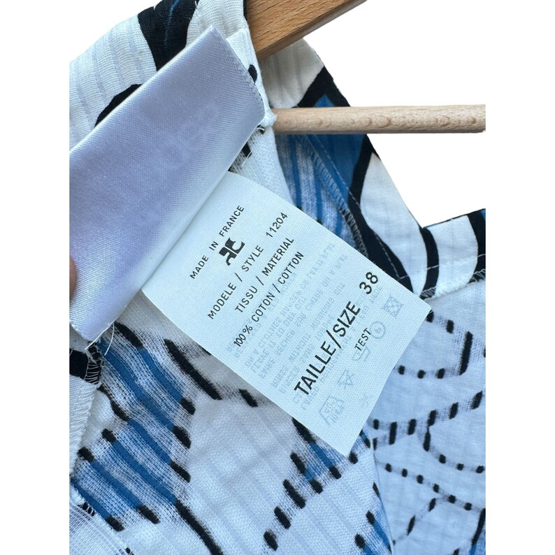 Puede incluir: Top de algod&oacute;n blanco y azul con estampado, con una etiqueta blanca que dice "Made in France", "Tissu / Material", "Modele / Style 11204", "100% Coton / Cotton", y "Taille / Size 38".