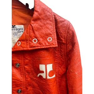 May include: A bright orange leather jacket with a large white logo on the front. The jacket has a high collar and a button closure. The label on the inside of the jacket reads "C. P.  irreges Paris".