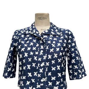 K&ouml;nnte beinhalten: Marineblaue Jacke mit wei&szlig;em Kreuzmuster. Die Jacke hat einen Kragen, Dreiviertel&auml;rmel und wei&szlig;e Kn&ouml;pfe vorne. Die Jacke wird auf einer Schneiderpuppe pr&auml;sentiert.