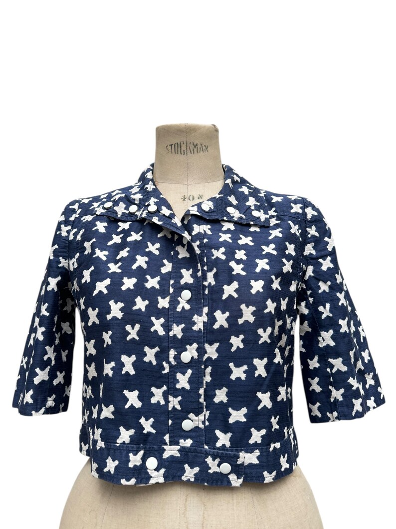 K&ouml;nnte beinhalten: Marineblaue Jacke mit wei&szlig;em Kreuzmuster. Die Jacke hat einen Kragen, Dreiviertel&auml;rmel und wei&szlig;e Kn&ouml;pfe vorne. Die Jacke wird auf einer Schneiderpuppe pr&auml;sentiert.