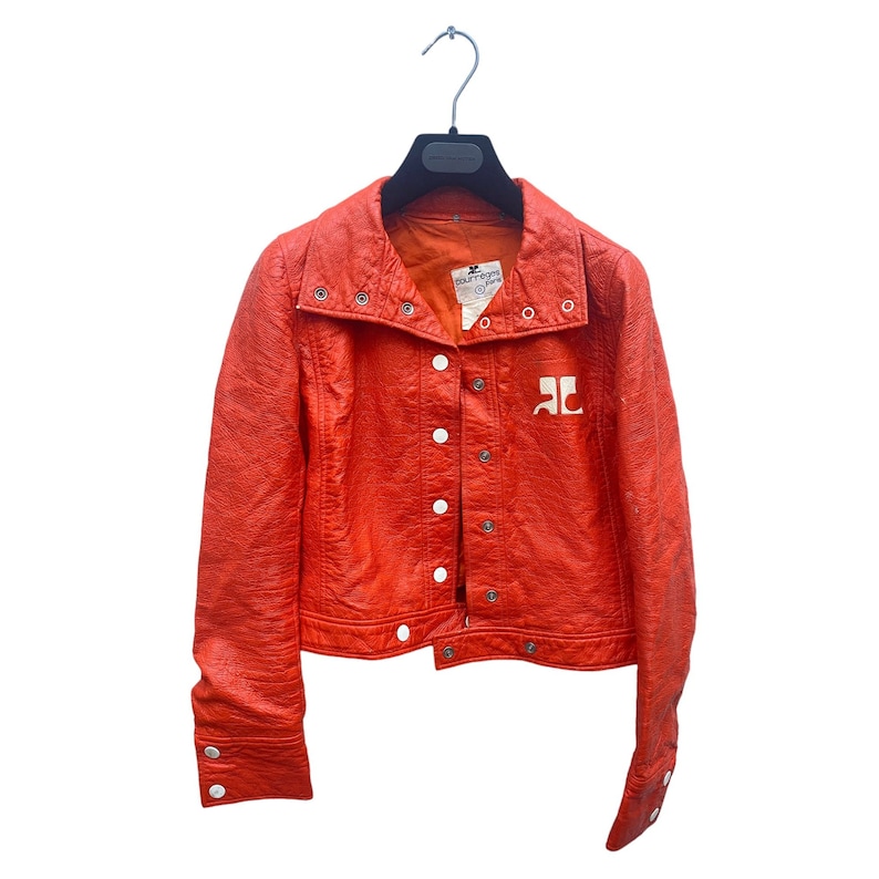 May include: A bright orange leather jacket with a white logo on the front. The jacket has a snap closure and a collar that can be folded down.
