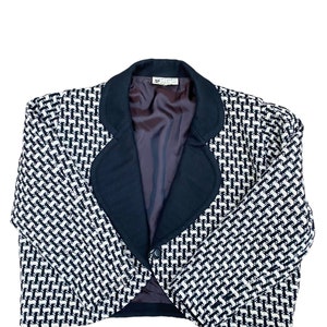 May include: A cropped blazer in a black and white patterned fabric, featuring a black collar and a single button fastening. The blazer is made from a textured material.