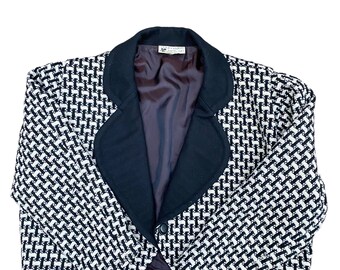 May include: A black and white patterned cropped blazer with a black collar and a single button closure. The blazer is made of a textured fabric.