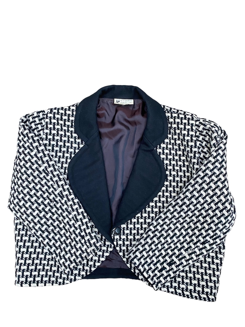 May include: A cropped blazer in a black and white patterned fabric, featuring a black collar and a single button fastening. The blazer is made from a textured material.