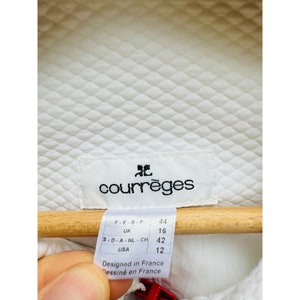Puede incluir: Etiqueta blanca Courr&egrave;ges con texto negro y tabla de tallas. La etiqueta dice "Courr&egrave;ges" en negro. La tabla de tallas muestra las tallas para Francia, Reino Unido y Estados Unidos. La etiqueta est&aacute; dise&ntilde;ada en Francia.