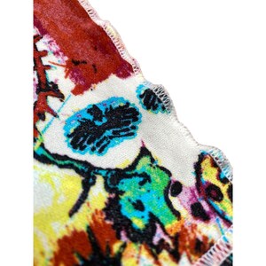 Może przedstawiać: Zbliżenie tkaniny z kolorowym, abstrakcyjnym wzorem kwiatowym. Wz&oacute;r zawiera mieszankę odcieni czerwieni, ż&oacute;łci, niebieskiego i zieleni na białym tle. Krawędź tkaniny ma falisty brzeg.