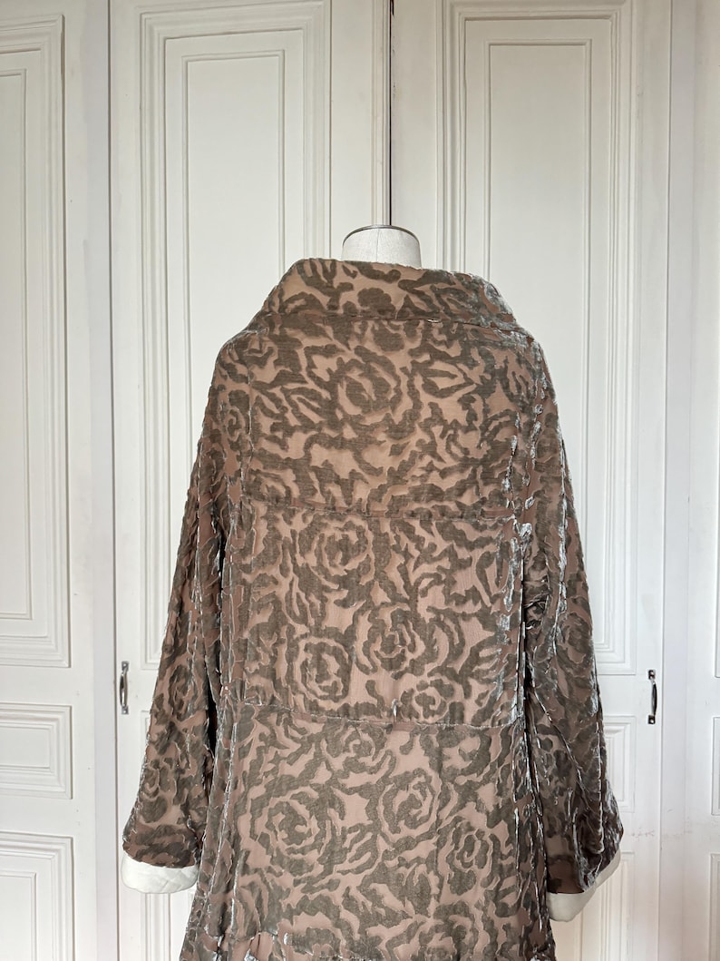 Puede incluir: Un abrigo largo marr&oacute;n con un dise&ntilde;o floral, exhibido en un maniqu&iacute;. Las mangas son largas, con pu&ntilde;os blancos. El abrigo tiene un cuello grande y cierre de botones. La tela parece ser terciopelo.