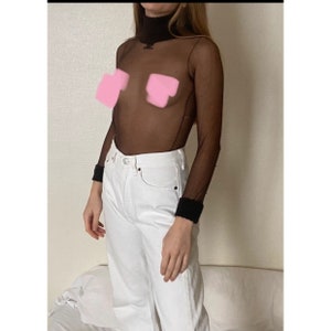 Op de afbeelding: Een zwart doorschijnend turtleneck-top met lange mouwen en een zwarte afwerking aan de manchetten. De top wordt gedragen over een witte jeans.
