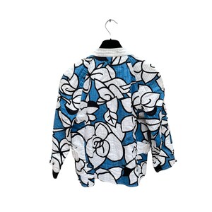K&ouml;nnte beinhalten: Eine Jacke mit blauem und wei&szlig;em Blumendruck und gesteppter Textur. Die Jacke hat einen Stehkragen und lange &Auml;rmel.