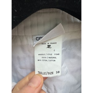 K&ouml;nnte beinhalten: Ein wei&szlig;es Kleidungsetikett mit schwarzem Text, der "MADE IN FRANCE" und "C" lautet. Unter dem Text befindet sich ein Logo eines stilisierten "C". Unter dem Logo befindet sich weiterer schwarzer Text, der "MODELE / STYLE 11048", "TISSU / MATERIAL" und "100% COTON / COTTON" lautet. Unter diesem Text befindet sich ein wei&szlig;es Etikett mit schwarzem Text, der "TAILLE / SIZE 38" lautet.