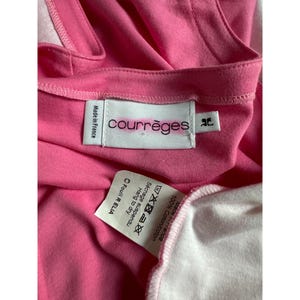 May include: Close-up of a pink garment with the brand label "Courr&egrave;ges" visible. The label indicates the item is made in France and is 100% cotton. Additional care instructions are also printed on the label.