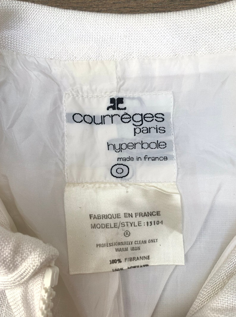May include: White label with black text reading "ac courreges paris hyperbole made in france" and a circle symbol. Below is a white label with black text reading "FABRIQUE EN FRANCE MODELE/STYLE: 15104 A PROFESSIONNALLY CLEAN ONLY WARM IRON 100% FIBRANNE".