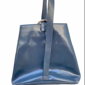 May include: A dark blue leather tote bag with a silver ring handle and a long strap.