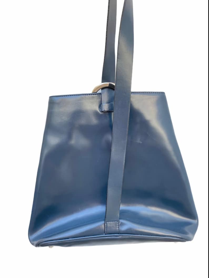 May include: A dark blue leather tote bag with a silver ring handle and a long strap.