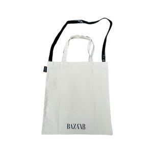 May include: A white canvas tote bag with black straps and the word "BAZAAR" printed on the front.