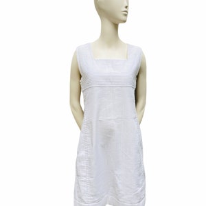 May include: A white sleeveless dress with thin vertical stripes. The dress has a square neckline and a straight, A-line silhouette.