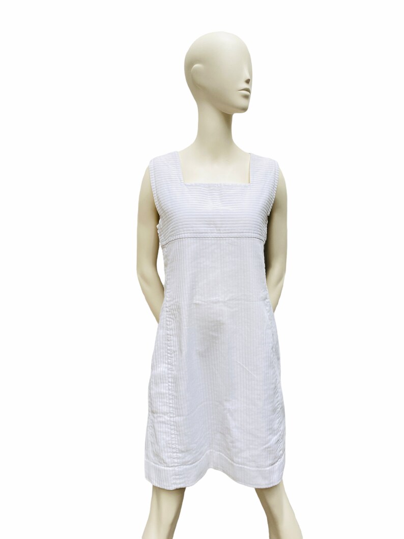May include: A white sleeveless dress with thin vertical stripes. The dress has a square neckline and a straight, A-line silhouette.