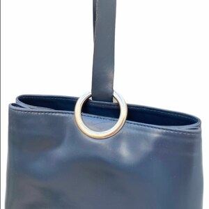 May include: A dark blue leather tote bag with a silver ring handle.