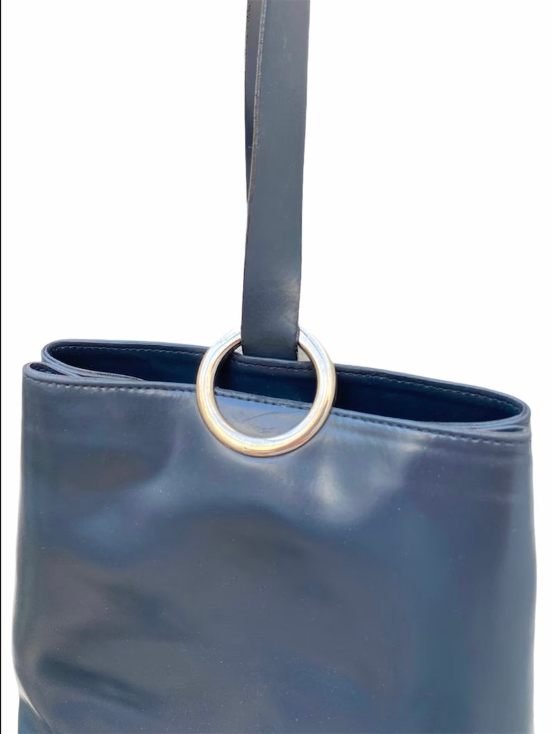 May include: A dark blue leather tote bag with a silver ring handle.