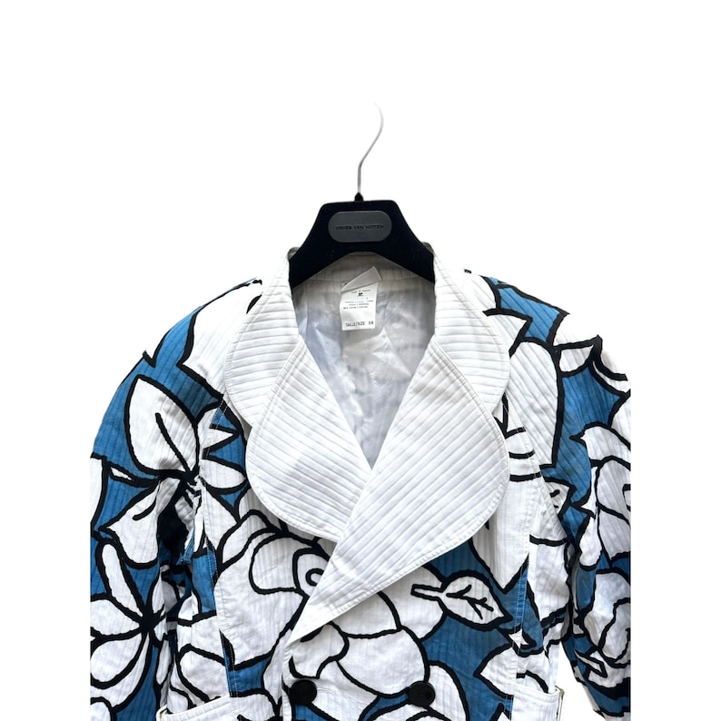 K&ouml;nnte beinhalten: Eine Jacke mit wei&szlig;em und blauem Blumendruck, wei&szlig;em Kragen und doppelreihigem Verschluss. Die Jacke tr&auml;gt ein "Marc Jacobs"-Etikett.