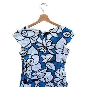 Puede incluir: Un vestido de estampado floral azul y blanco con mangas cortas y cuello redondo. El vestido est&aacute; colgado en una percha de madera.