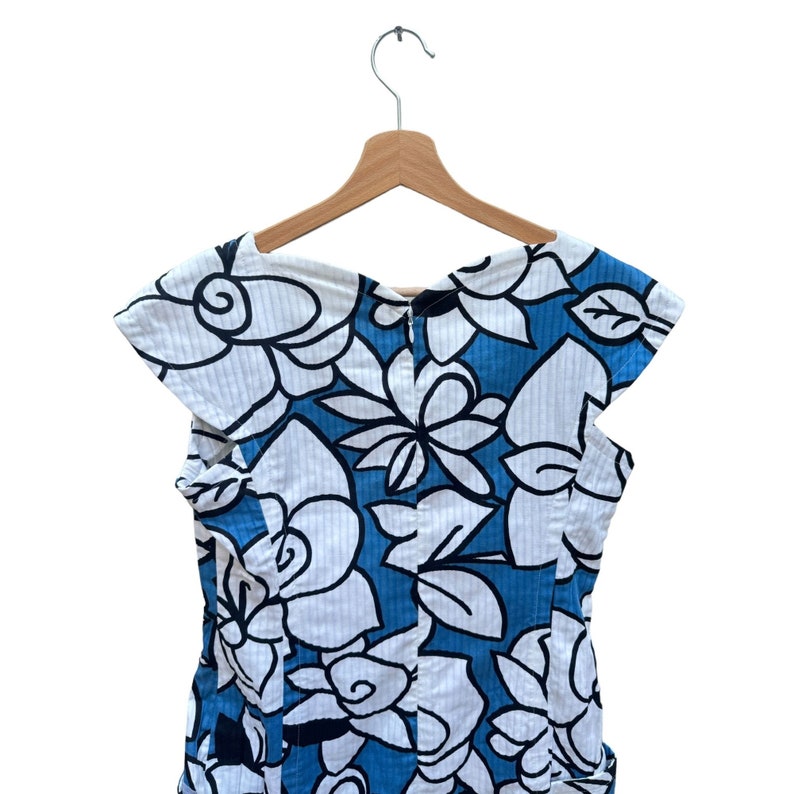 Puede incluir: Un vestido de estampado floral azul y blanco con mangas cortas y cuello redondo. El vestido est&aacute; colgado en una percha de madera.