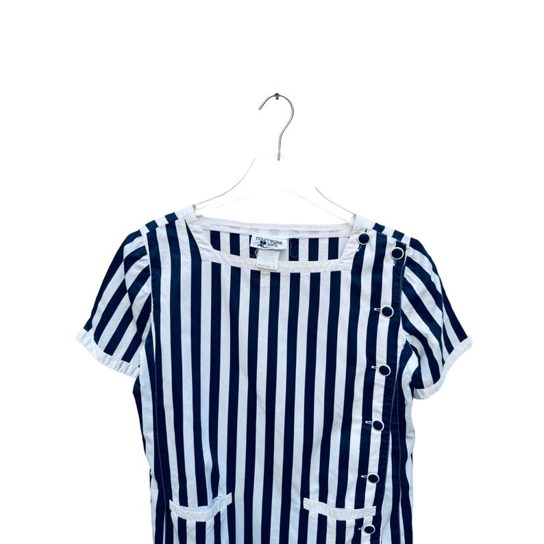 May include: A black and white striped short-sleeved dress with a button detail on the side. The dress has a scoop neck and a relaxed fit.