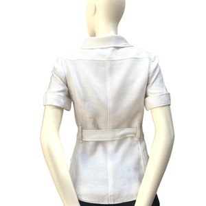 May include: A white linen shirt with short sleeves and a belt. The shirt has a collar and a button-up front.
