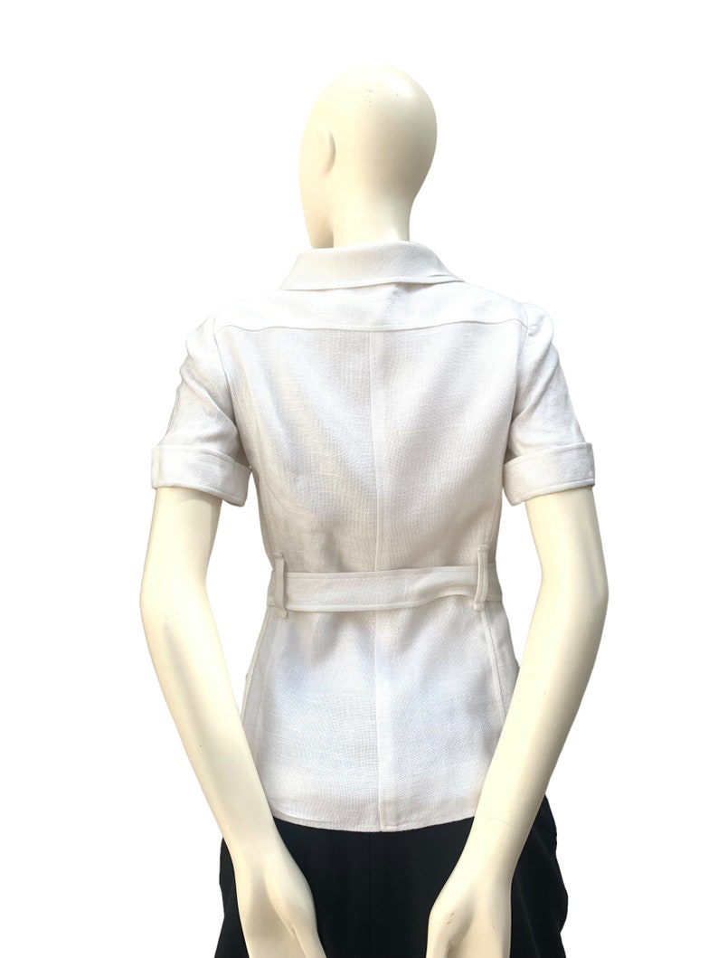 May include: A white linen shirt with short sleeves and a belt. The shirt has a collar and a button-up front.