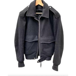 Peut inclure: Une veste bomber en laine noire avec une fermeture éclair et deux grandes poches. La veste a un col et des poignets côtelés.