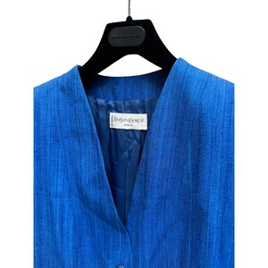 May include: A blue linen blazer with a V-neck and a single button closure. The label reads "Yves Saint Laurent" and "Rive Gauche".