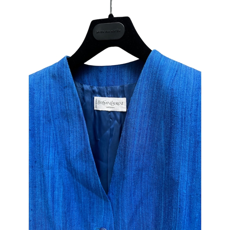 May include: A blue linen blazer with a V-neck and a single button closure. The label reads "Yves Saint Laurent" and "Rive Gauche".