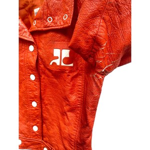 May include: A bright orange leather jacket with a white logo that says "RC" on the front. The jacket has a zipper closure and a collar.