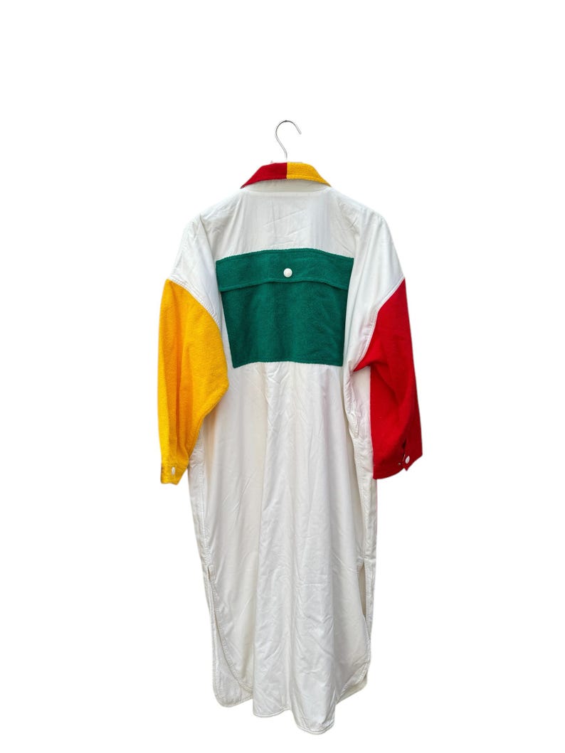 Puede incluir: Una camisa blanca de manga larga con un dise&ntilde;o de bloques de color verde, amarillo y rojo. La camisa tiene un cuello abotonado y un bolsillo de parche en la espalda.