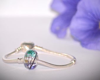 May include: A silver charm bracelet with a green, blue, and black glass bead. The bead has a swirling pattern inside.