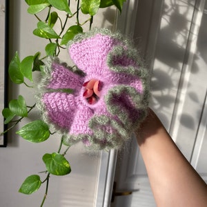 May include: A pink and green crocheted flower with a ruffled edge.