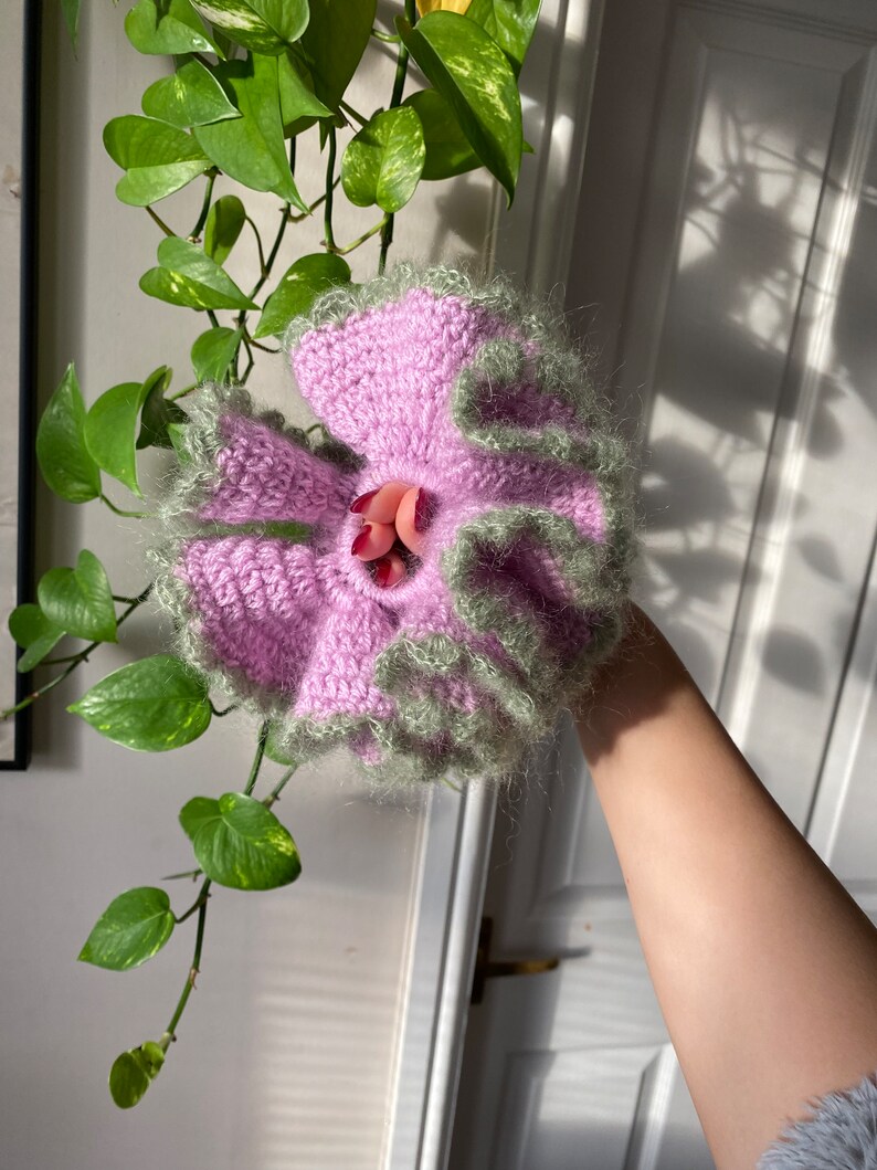 May include: A pink and green crocheted flower with a ruffled edge.