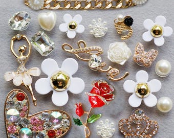 May include: A collection of decorative shoe charms featuring various designs including a gold chain, white flowers with gold centers, a ballerina, a red rose, a heart filled with colorful crystals, a crown, a butterfly, and the word love in gold.