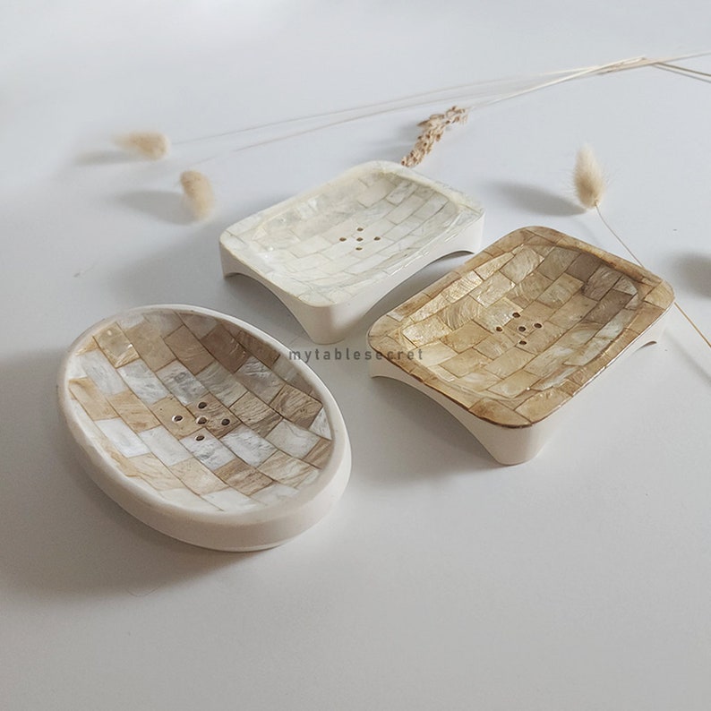 Puede incluir: Tres jaboneras decorativas hechas de materiales naturales. Las jaboneras son de forma rectangular y ovalada. Las jaboneras est&aacute;n hechas de un material de color marr&oacute;n claro y blanco que parece paja o madera tejida.