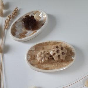Puede incluir: Dos platos ovalados de cer&aacute;mica beige y blanca con bordes elevados. Un plato tiene una pastilla de jab&oacute;n marr&oacute;n en forma de estrella. El otro plato tiene dos pastillas de jab&oacute;n beige en forma de estrella.