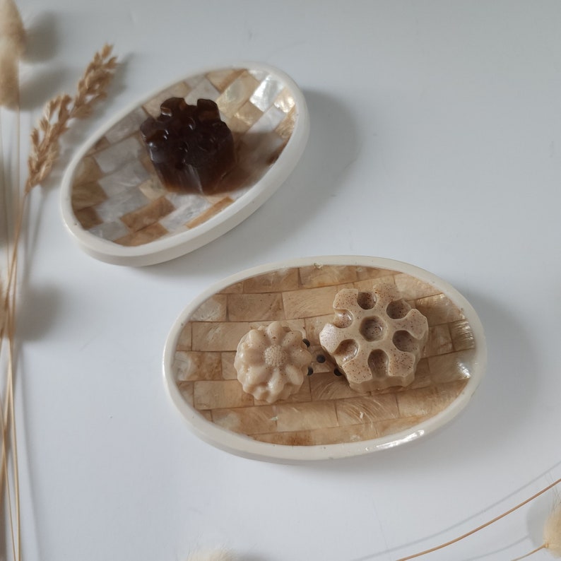 Puede incluir: Dos platos ovalados de cer&aacute;mica beige y blanca con bordes elevados. Un plato tiene una pastilla de jab&oacute;n marr&oacute;n en forma de estrella. El otro plato tiene dos pastillas de jab&oacute;n beige en forma de estrella.