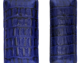 Puede incluir: Dos estuches para cigarros de cuero azul con un patrón de cocodrilo. Los estuches tienen el texto "Tobacco Road" grabado en relieve en la parte delantera.