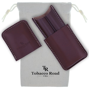 May include: A brown leather cigar case with a Tobacco Road logo. The case is closed and comes with a white canvas drawstring bag.