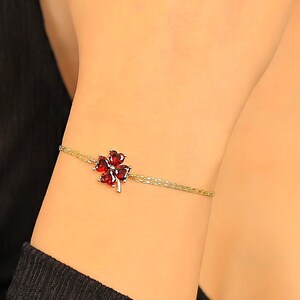 Puede incluir: Un brazalete de cadena dorada con un dije de trébol de cuatro hojas rojo.
