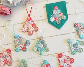 Könnte beinhalten: Eine Sammlung handgefertigter Weihnachtsbaumschmucke und ein Banner aus Stoff. Die Ornamente bestehen aus Patchwork-Stoff in verschiedenen Blumen- und Vichy-Mustern mit roten, blauen und grünen Akzenten. Jeder Baum hat ein Band zum Aufhängen. Das Banner ist aus türkisfarbenem Filz mit einem Patchwork-Baum.