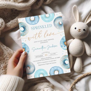 May include: A baby shower invitation featuring a watercolor design of blue donuts with sprinkles. The invitation reads "Sprinkled with love" and includes details for Samantha Jackson's baby shower, including the date, time, and location.