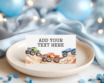 May include: A rectangular card featuring a watercolor illustration of three monster trucks in green, orange, and blue driving over rocky terrain. The text ADD YOUR TEXT HERE is printed in dark gray block letters at the top center of the card.