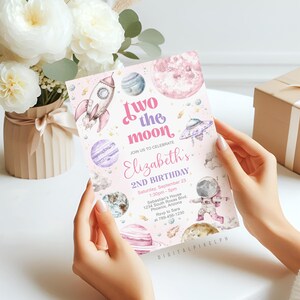 May include: A pink and white invitation card with a space theme, featuring a rocket, planets, and an astronaut. The text reads "Two the Moon" and announces a 2nd birthday party for Elizabeth.
