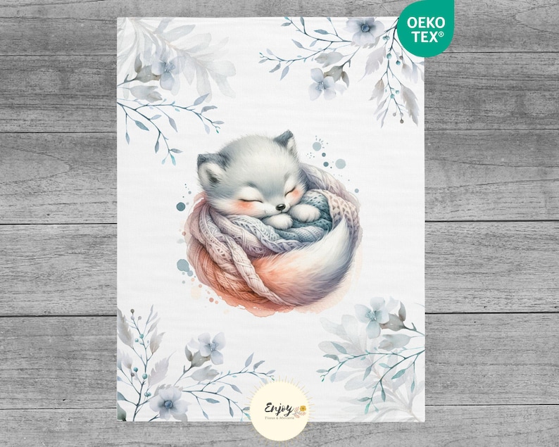 May include: A watercolor illustration of a white fox curled up asleep in a cozy, gray and pink knitted blanket. The fox is surrounded by delicate, light blue watercolor flowers and leaves. The image has the text "Oeko Tex&reg;" in the top right corner and "Enjoy" in the bottom center.