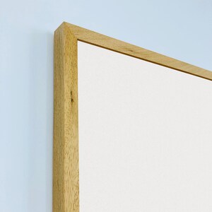 May include: Close-up of the top corner of a light wood picture frame. The frame is made of natural wood with a smooth finish. The frame is empty and ready to be filled with a picture or artwork.